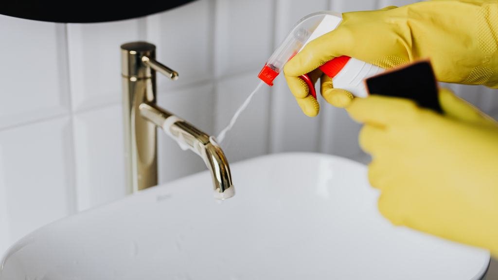 Gloved hand disinfecting a bathroom faucet
